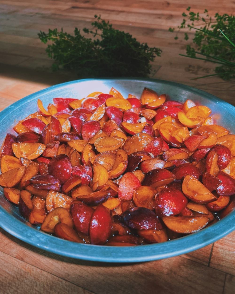 A bowl of halved stone fruit with garden herbs
